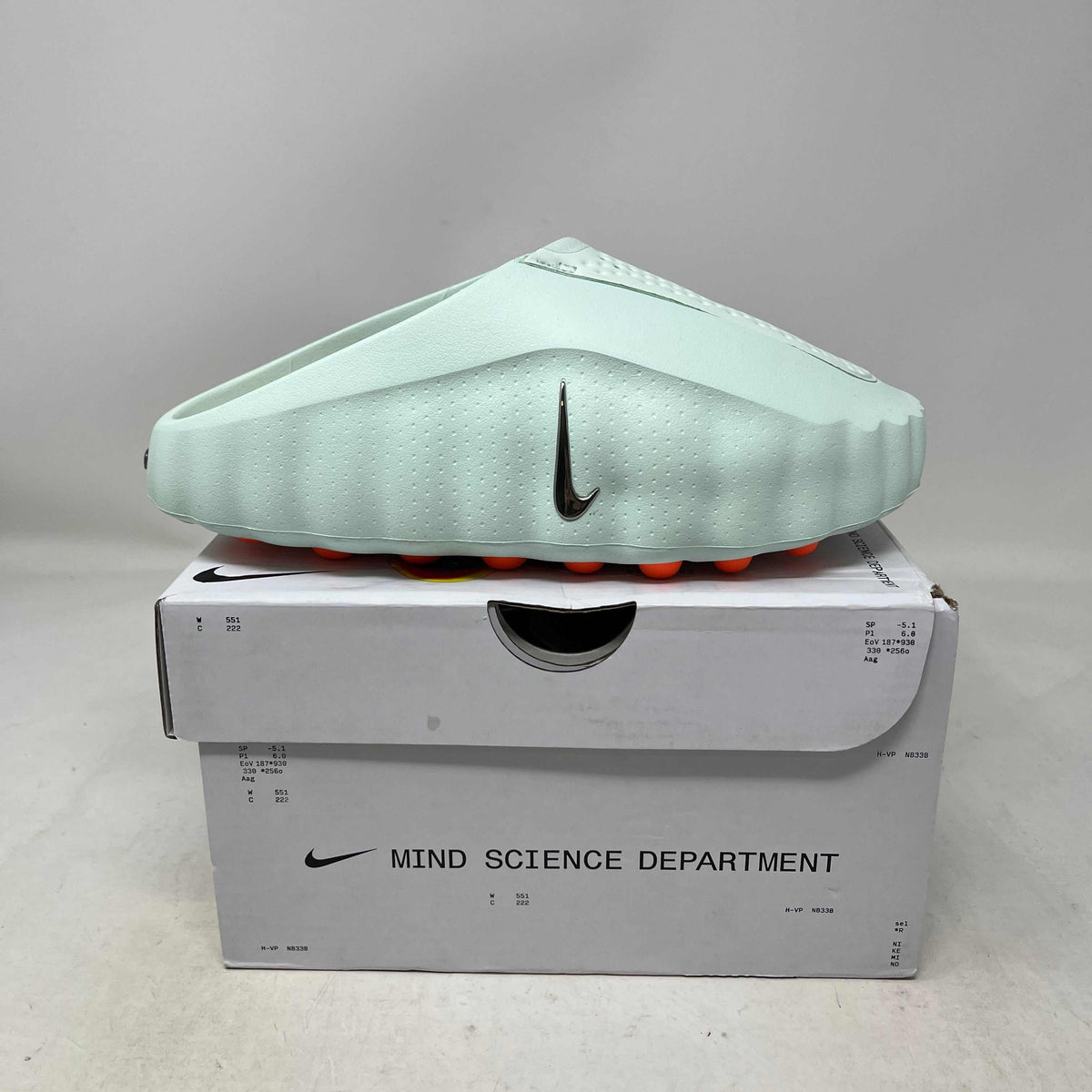 Nike Mind 001 Slide in pale green molded foam, with a textured upper, black Swoosh and bright orange sole pods.
