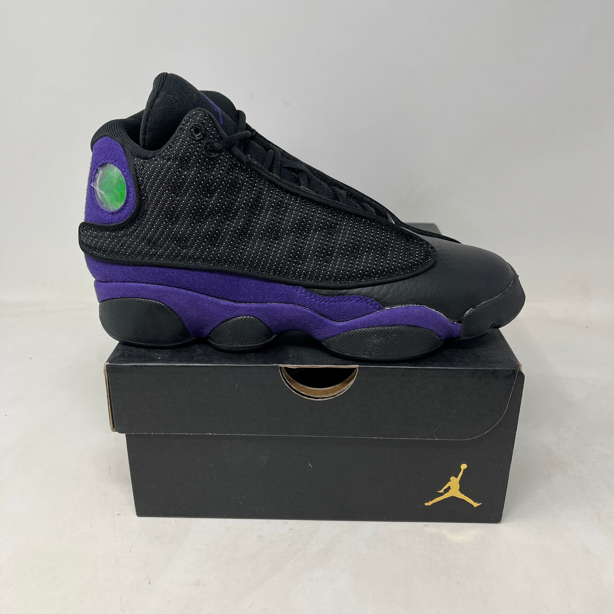 Jordan 13 Retro Court Purple sneaker with a black textured upper, purple leather panels, and green holographic heel detail.