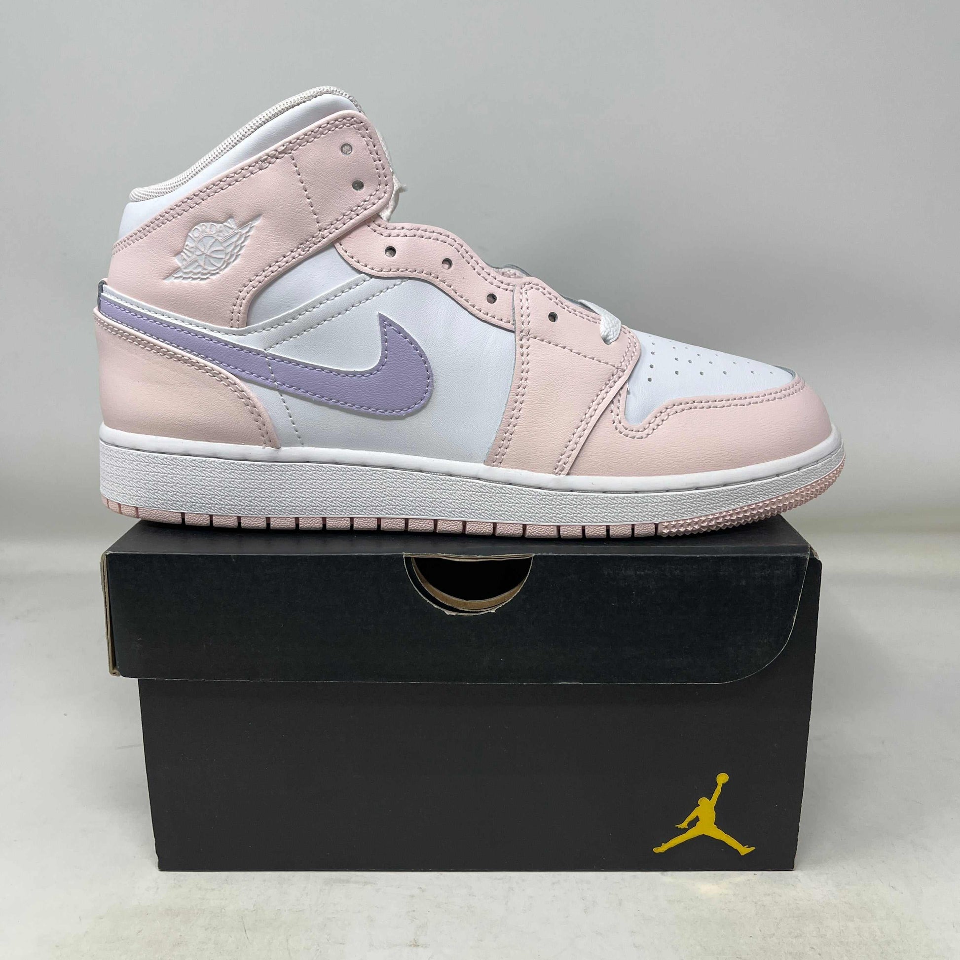 Jordan 1 Mid Pink Wash GS sneaker in pink, white, and lavender on a black Jordan box.