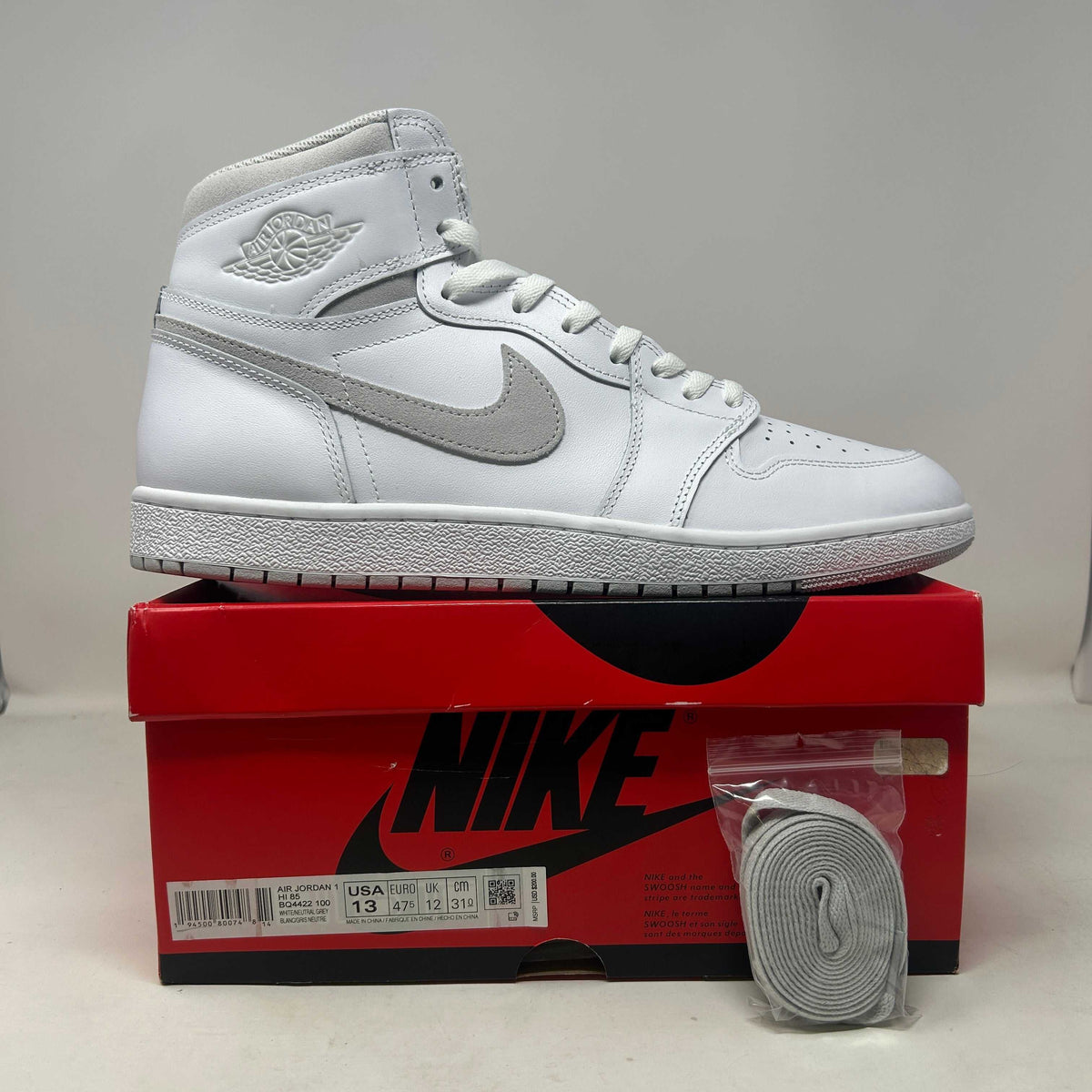 Jordan 1 Retro High '85 sneaker in white leather with grey Swoosh, laces and Wings logo, high-top design
