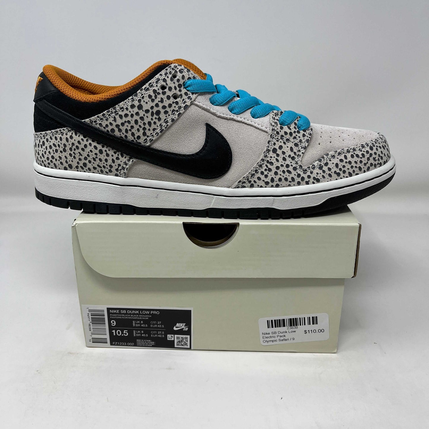 Nike SB Dunk Low Electric Pack Olympic Safari sneaker with black swoosh, spotted grey pattern, blue laces, and orange inner lining on a beige box