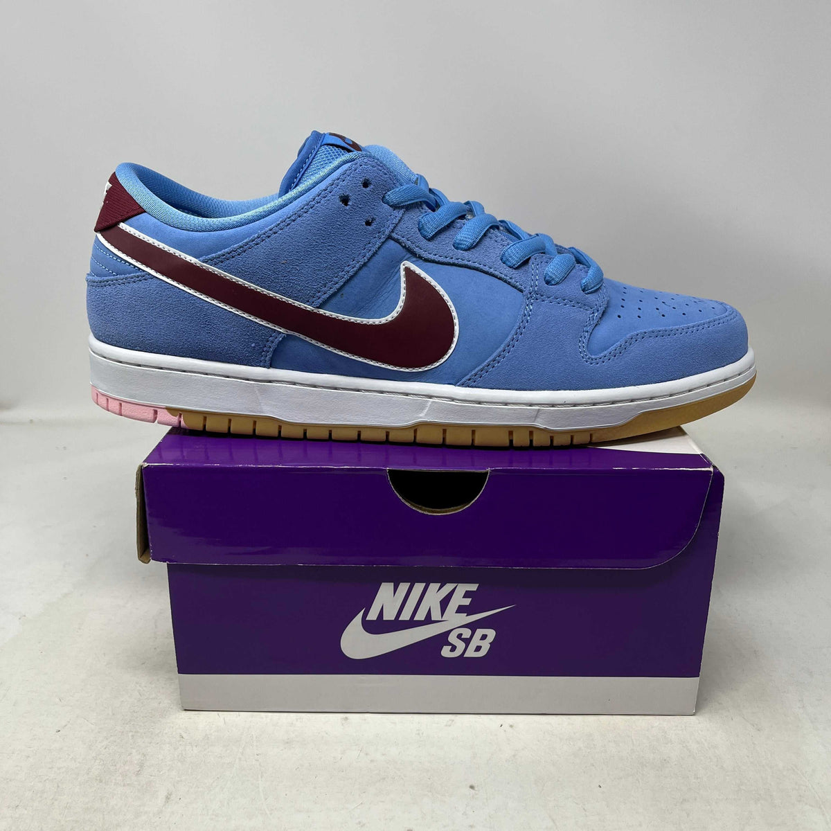 Nike SB Dunk Low sneaker in blue suede with maroon leather swoosh and white midsole on purple Nike SB box